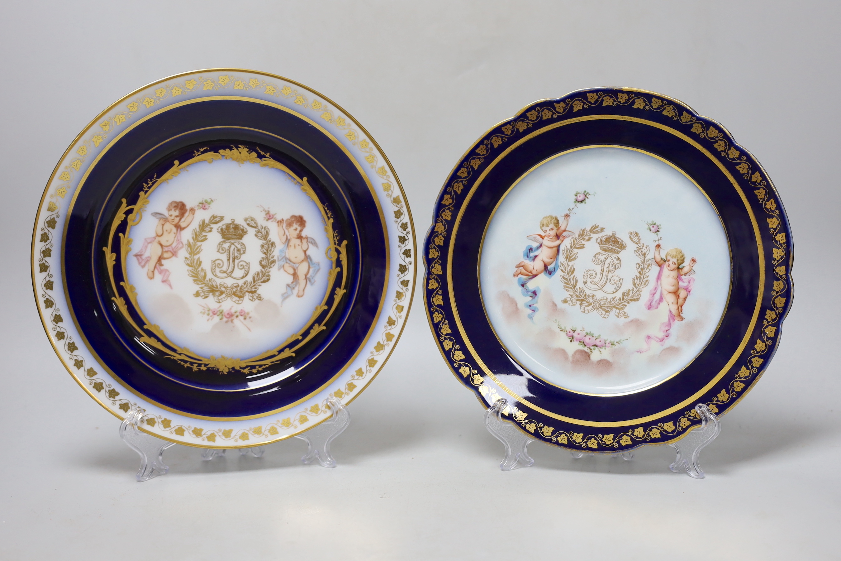Two similar Sevres style plates hand painted with putti and gilded ivy leaf design border, each stamped to the reverse, the largest 25cm in diameter